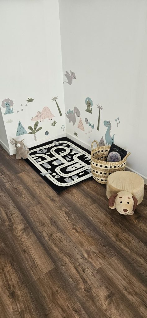 Rincón infantil con alfombra de carreteras, peluches y vinilos de dinosaurios en la pared