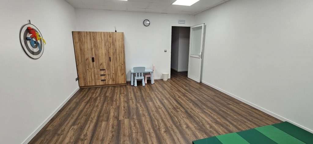 Sala amplia con mesa y sillas infantiles, armario de madera y colchonetas en el suelo